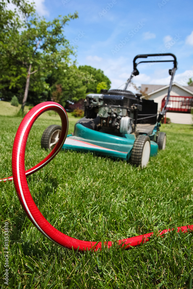Fototapeta premium Lawnmower in backyard with red hose on grass in front