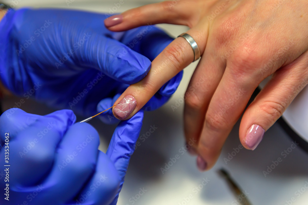 Fototapeta premium Manicurist painting nails to female client, close-up. Beautician doing art design on nails. Professional hand and nail care in beauty salon.