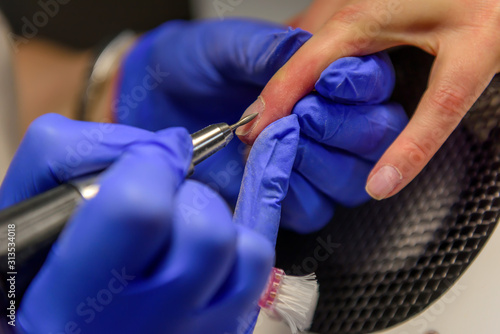 Apparatus manicure  close-up. Gentle nail care. Manicurist in blue gloves removes the cuticle with a cutter.