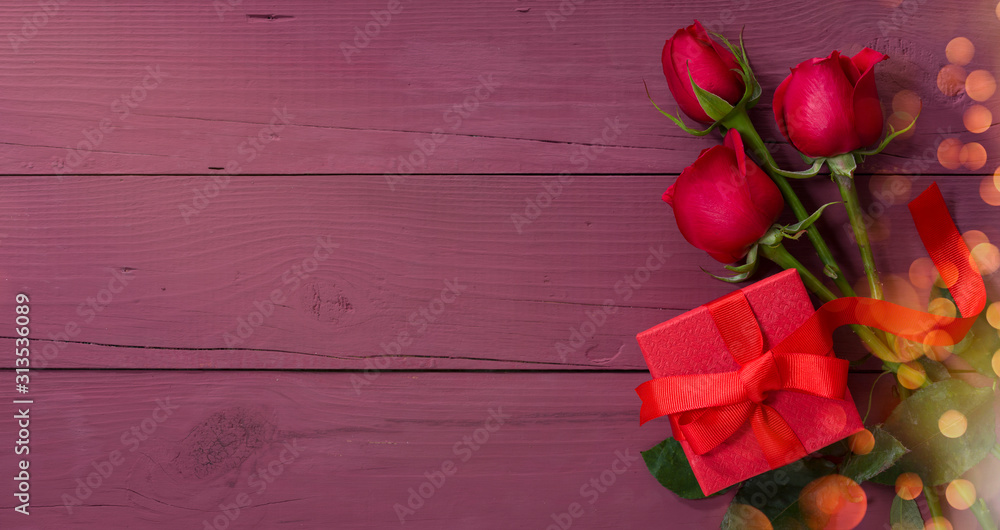 Valentines day card. Red gift box and roses on purple wooden table