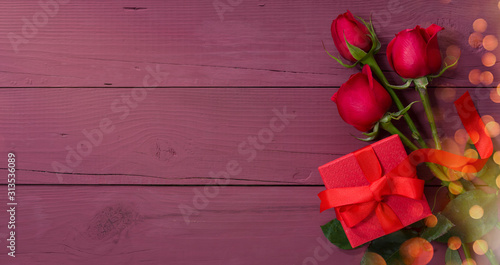 Valentines day card. Red gift box and roses on purple wooden table