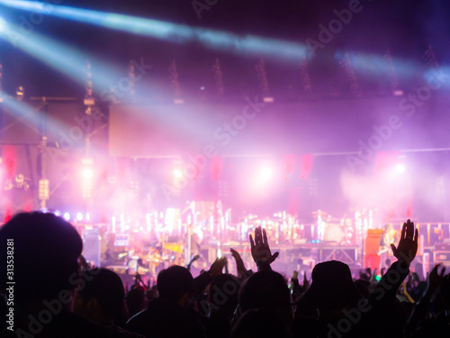 crowd at concert - summer music festival in front of bright stage lights. Dark background, smoke, concert spotlights.people dancing and having fun in summer festival