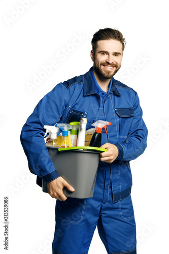 Attractive young man  in cleaning uniform holding  a bucket of cleaning products in his hands, isolated on white background.
