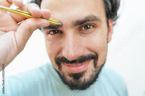 Portrait of a handsome young latin man tweezing eyebrows, skin care, beauty procedures for men concept.