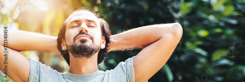 A bearded man is meditating outdoor in the park with face raised up to sky and eyes closed on sunny summer day. Concept of meditation, dreaming, wellbeing healthy lifestyle