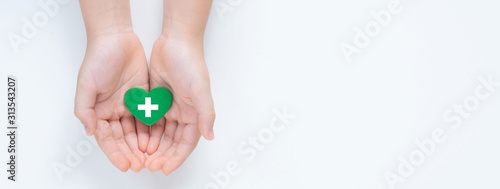 Hands holding a beautiful green heart with hospital white cross symbol on it showing a concept of Health care service, cancer treatment and heart surgery. Banner top view Isolated on white background. photo