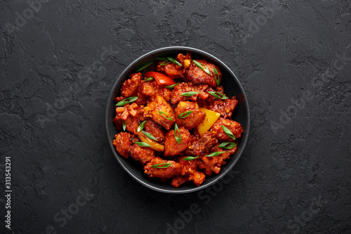 Fish Manchurian dry looks like Schezwan Fish in black bowl at dark slate background. Fish Manchurian - is indo chinese cuisine dish with deep fried salmon, bell peppers, sauce and onion. Top view photo