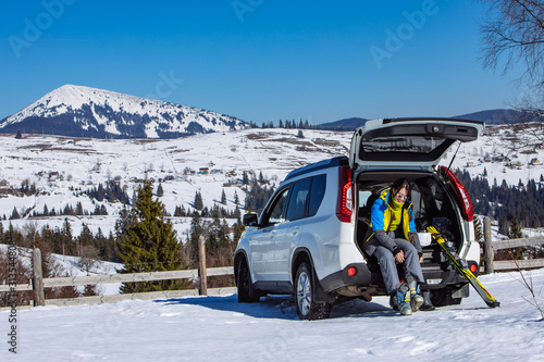 woman changing boots to ski sitting in car trunk. sunny day