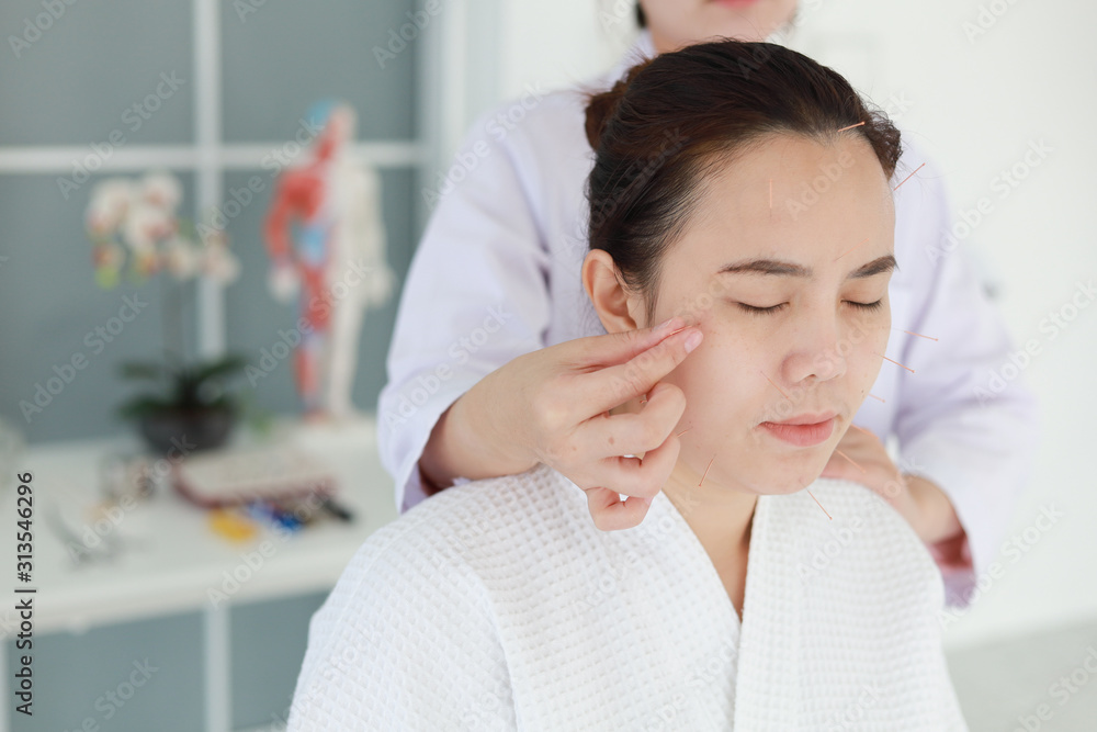 hand of doctor performing acupuncture therapy . Asian female undergoing acupuncture treatment with a line of fine needles inserted into the her face skin in clinic hospital hand of doctor performing acupuncture therapy . Asian female undergoing acupuncture treatment with a line of fine needles inserted into the her face skin in clinic hospital