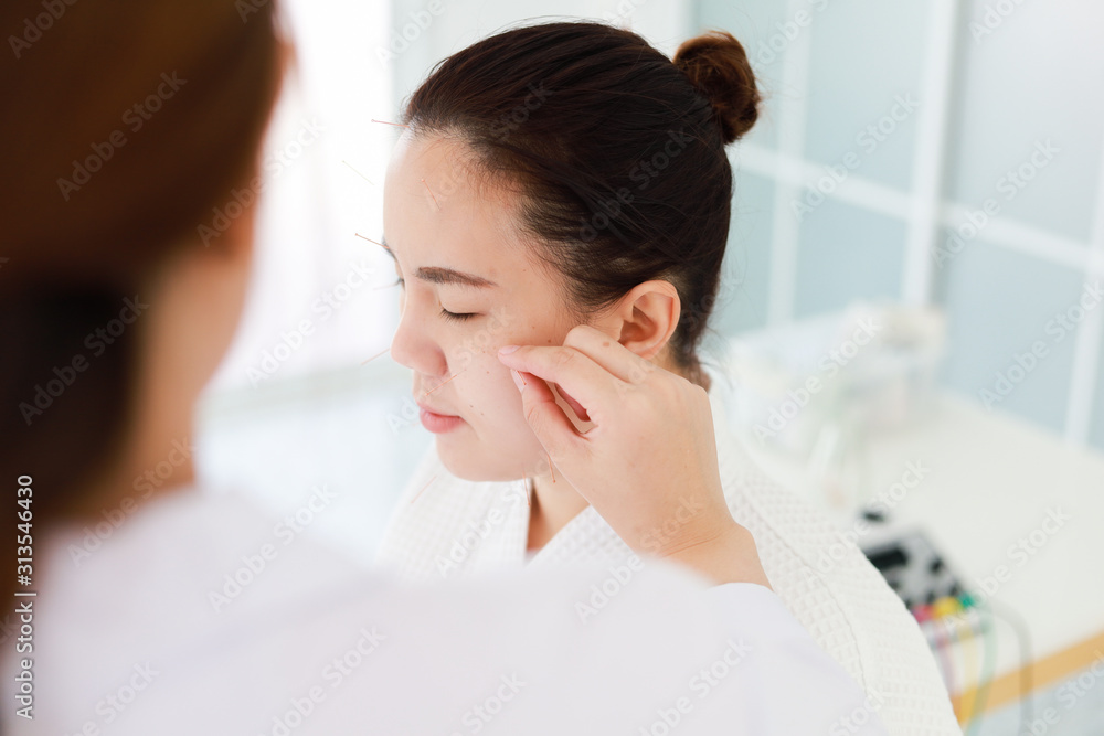 hand of doctor performing acupuncture therapy . Asian female undergoing acupuncture treatment with a line of fine needles inserted into the her face skin in clinic hospital hand of doctor performing acupuncture therapy . Asian female undergoing acupuncture treatment with a line of fine needles inserted into the her face skin in clinic hospital