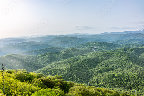 Layers of mountains in the haze during sunset. Beautiful sunset in the mountains. Beautiful sunset in a green hilly valley with villages and fog in the lowlands.