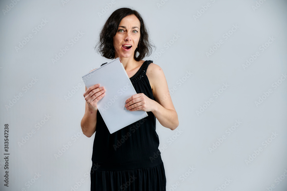 Portrait of a pretty brunette woman in a black dress with a folder in her hands on a white background. Shows emotions with hands in different poses right in front of the camera. Portrait of a pretty brunette woman in a black dress with a folder in her hands on a white background. Shows emotions with hands in different poses right in front of the camera.