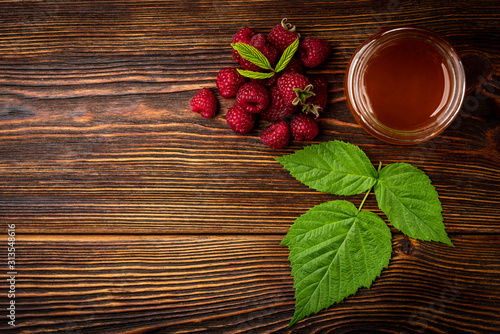  Honey in glass jar and fresh raspberry on dark wooden background.