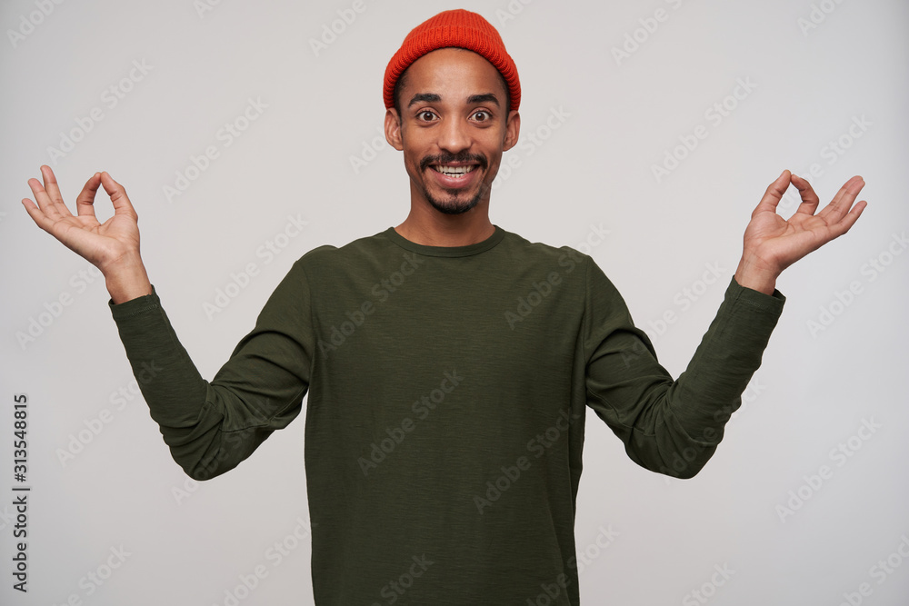 Indoor shot of cheerful attractive young brown-eyed dark skinned man with beard smiling widely at camera and raising hands with mudra sign, isolated over white background Indoor shot of cheerful attractive young brown-eyed dark skinned man with beard smiling widely at camera and raising hands with mudra sign, isolated over white background