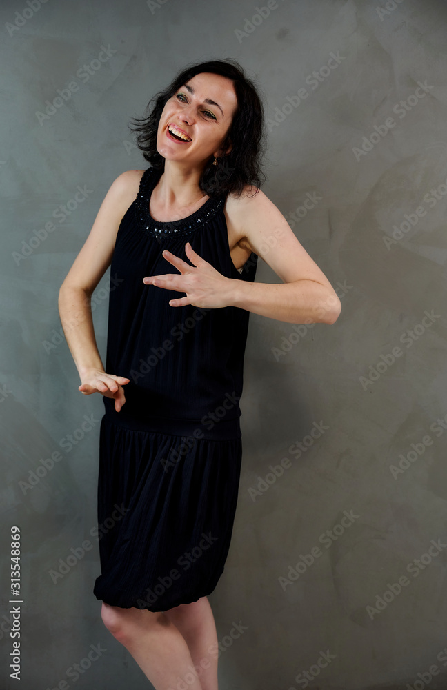 Full length portrait of a pretty emotional brunette woman in black dress on alternative gray background in vintage interior. Standing right in front of the camera. Full length portrait of a pretty emotional brunette woman in black dress on alternative gray background in vintage interior. Standing right in front of the camera.
