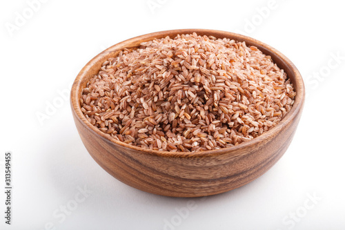 Wooden bowl with unpolished brown rice isolated on white background. Side view.