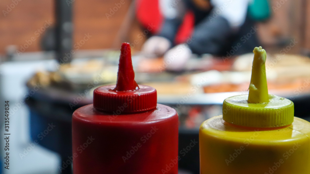 ketchup and mayonnaise in plastic tubes near a street grill in the foreground close-up with selective focus. Barbecue, street food festival. Two cans of meat sauces. Red and yellow container. ketchup and mayonnaise in plastic tubes near a street grill in the foreground close-up with selective focus. Barbecue, street food festival. Two cans of meat sauces. Red and yellow container.