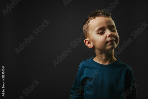 Child closed his eyes and dreams of not looking at camera isolated on blank gray studio background