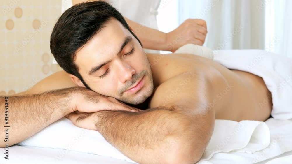 Smart man lying on spa bed.Poultice hot herbal massage at spa salon. Smart man lying on spa bed.Poultice hot herbal massage at spa salon.