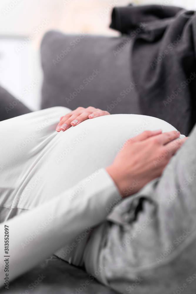 Fototapeta premium Pregnant tired exhausted woman with stomach issues at home on a couch, being sick.