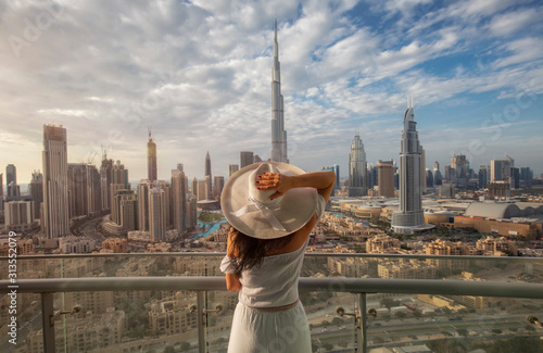 Tela Woman with a white hat is standing on a balcony in front of the skyline from Dub