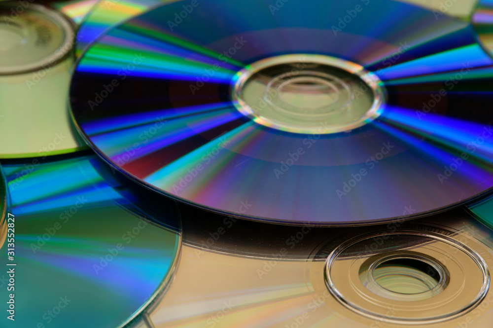 A purple, shiny cd on top of a desk and other cds