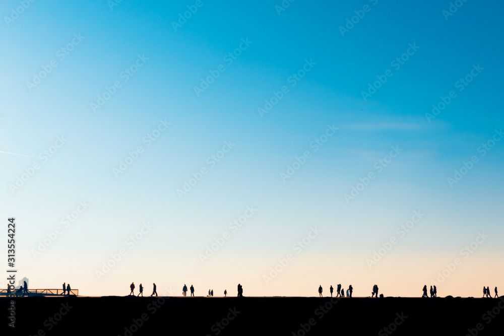 silhouettes of people coming and going on the shoreline against a big blue and orange sky at sunset