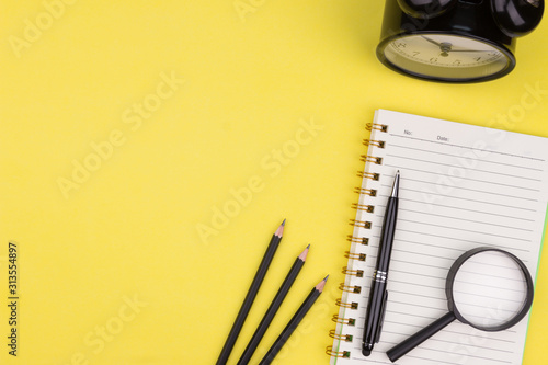 Education concept. Flat lay composition of open notebook, pen, magnifying glass, pencils and alarm clock. Copy space over green background. Top view on various stationery on desk. Creative workspace.