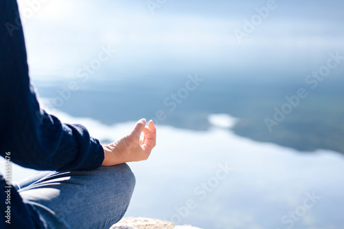 Woman doing yoga at sea beach. Blue background, copy space. Girl practicing meditating in lotus pose outdoors. Sport workout at nature. Female fitness classes, healthy lifestyle, wellbeing. Close up.