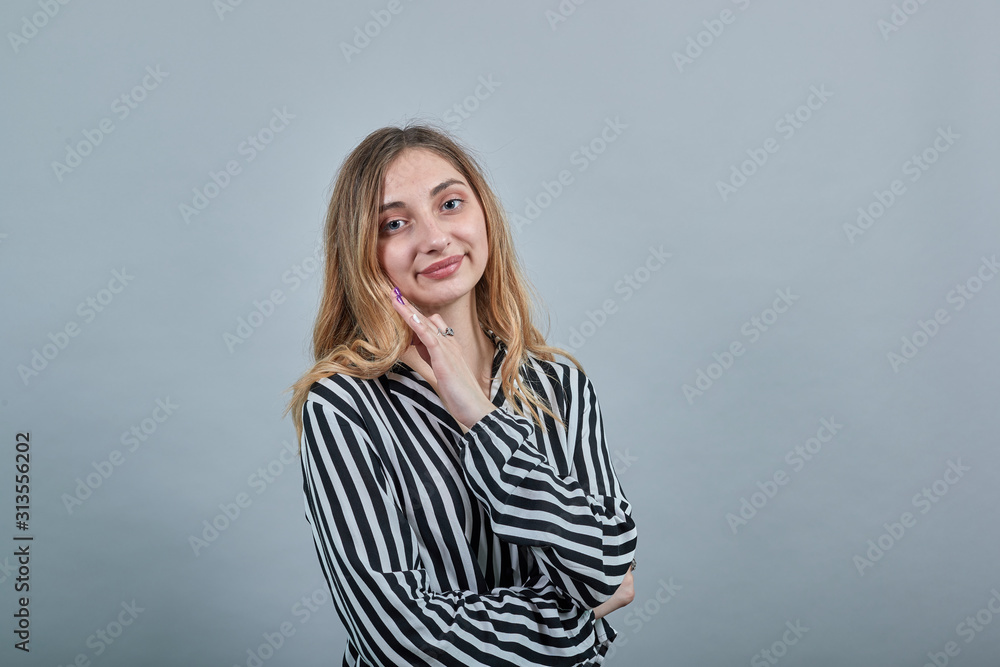 Pretty young woman in fashion black and white striped shirt looking at camera, keeping hand on cheek isolated on gray background in studio. People sincere emotions, lifestyle concept. Pretty young woman in fashion black and white striped shirt looking at camera, keeping hand on cheek isolated on gray background in studio. People sincere emotions, lifestyle concept.