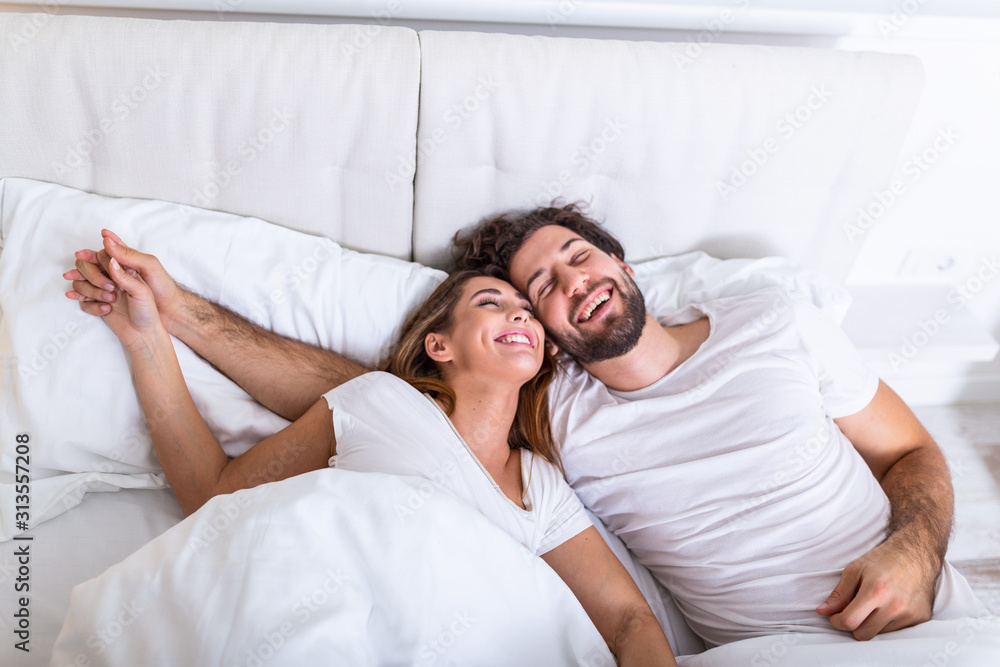 Young loving couple in the bed. Young couple lying in bed and laughing while tickling each other. Happy sensual young couple lying in bed together in the morning Young loving couple in the bed. Young couple lying in bed and laughing while tickling each other. Happy sensual young couple lying in bed together in the morning