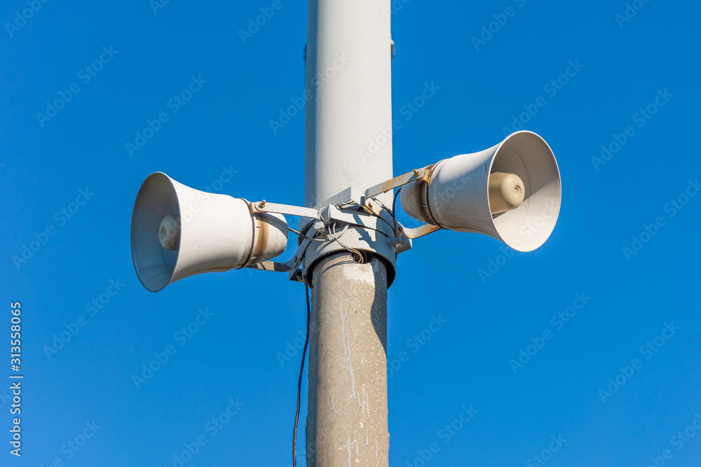 two loudspeakers on a street pole against a blue sky