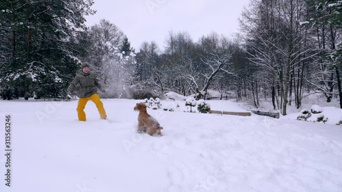The man and his dog, the red-haired cocker spaniel, frolic in the snow. Outdoor activities in the winter during a snowfall, a man and a companion dog play together, slow motion stock video