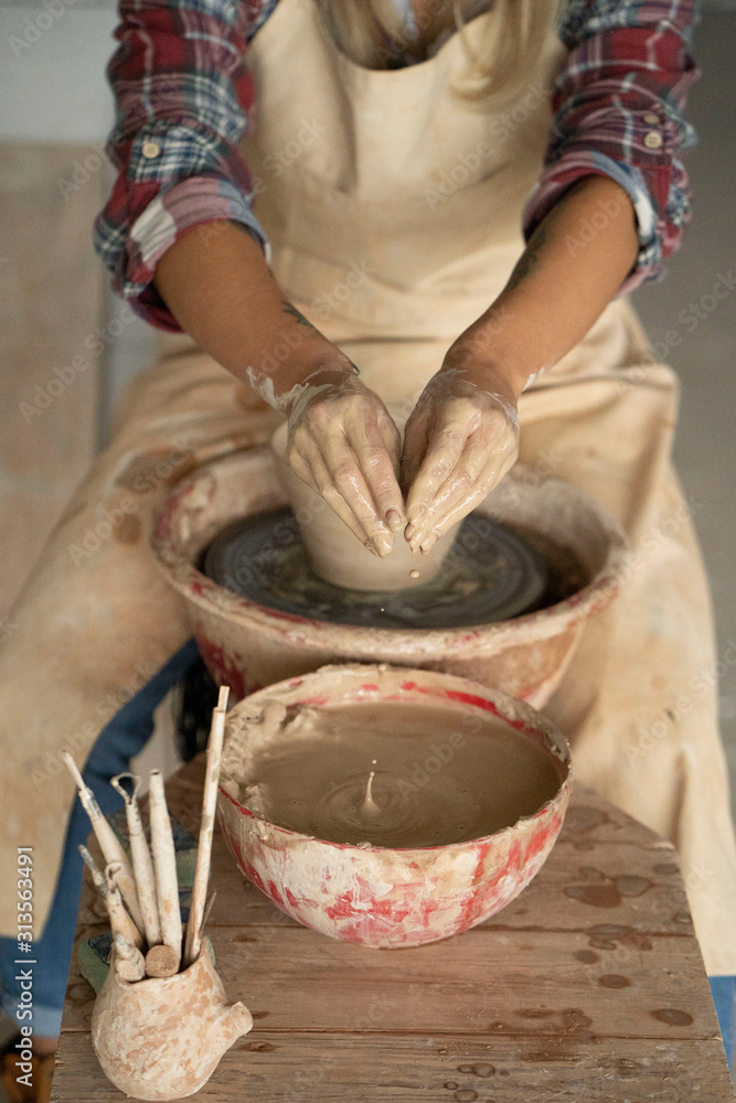 Close-up view of woman hands working on pottery wheel and making clay pot. Hands sculpts a cup from clay pot. Workshop on modeling on the potter's wheel.