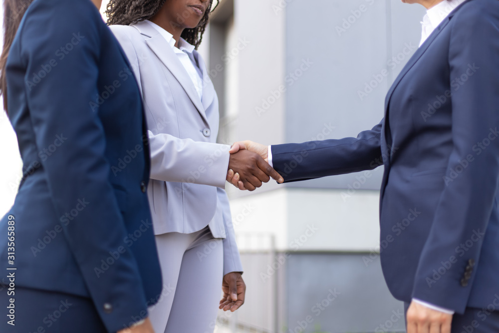 Interracial business ladies shaking hands near office building. Business women wearing office suits, meeting outside in city. Collaboration concept