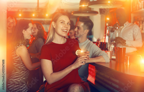 Cheerful girl with best friends partying in bar; dancing and toasting drinks