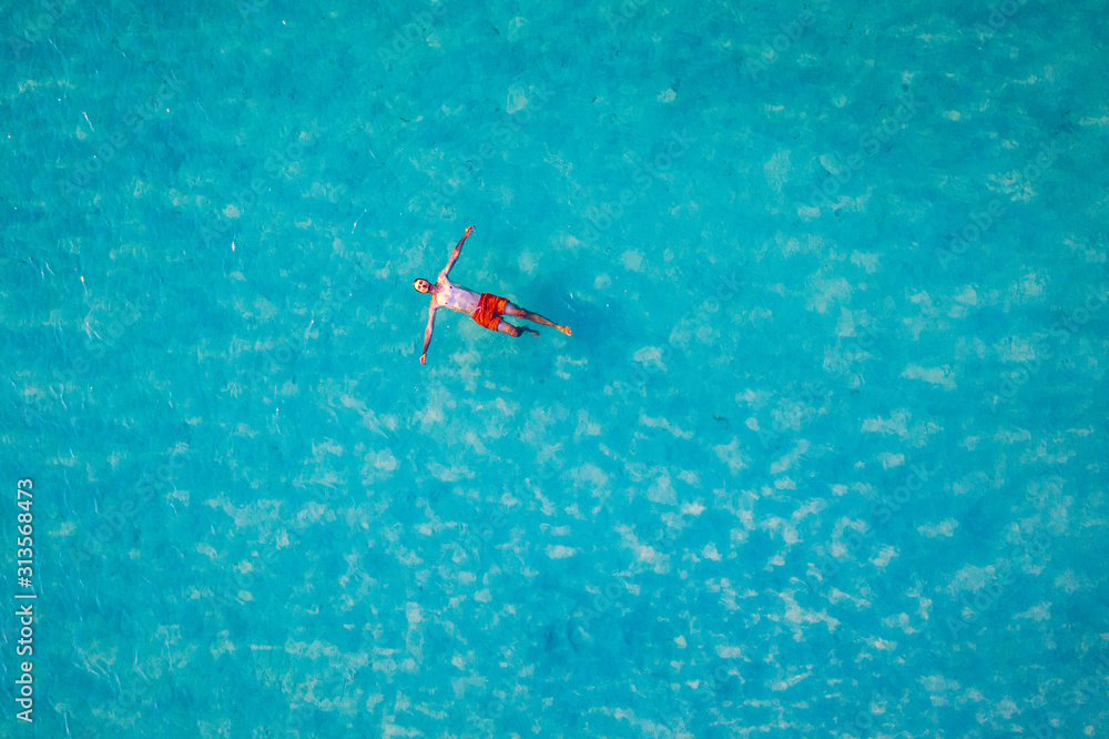 Drone view of a man floating in tropical sea water. Aerial view of young man floating on sea water enjoying sunbathing and vacations in tropical destination. People travel tourism holidays concept. Drone view of a man floating in tropical sea water. Aerial view of young man floating on sea water enjoying sunbathing and vacations in tropical destination. People travel tourism holidays concept.