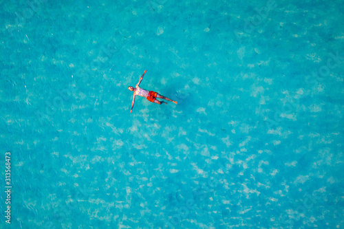 Drone view of a man floating in tropical sea water. Aerial view of young man floating on sea water enjoying sunbathing and vacations in tropical destination. People travel tourism holidays concept. © daliu