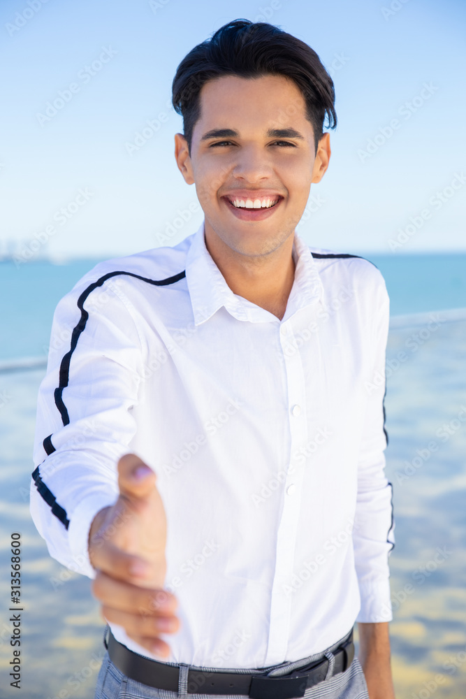 Cheerful guy posing outdoors. Young man making welcome inviting hand sign gesture or giving palm for handshake. Welcome concept Cheerful guy posing outdoors. Young man making welcome inviting hand sign gesture or giving palm for handshake. Welcome concept