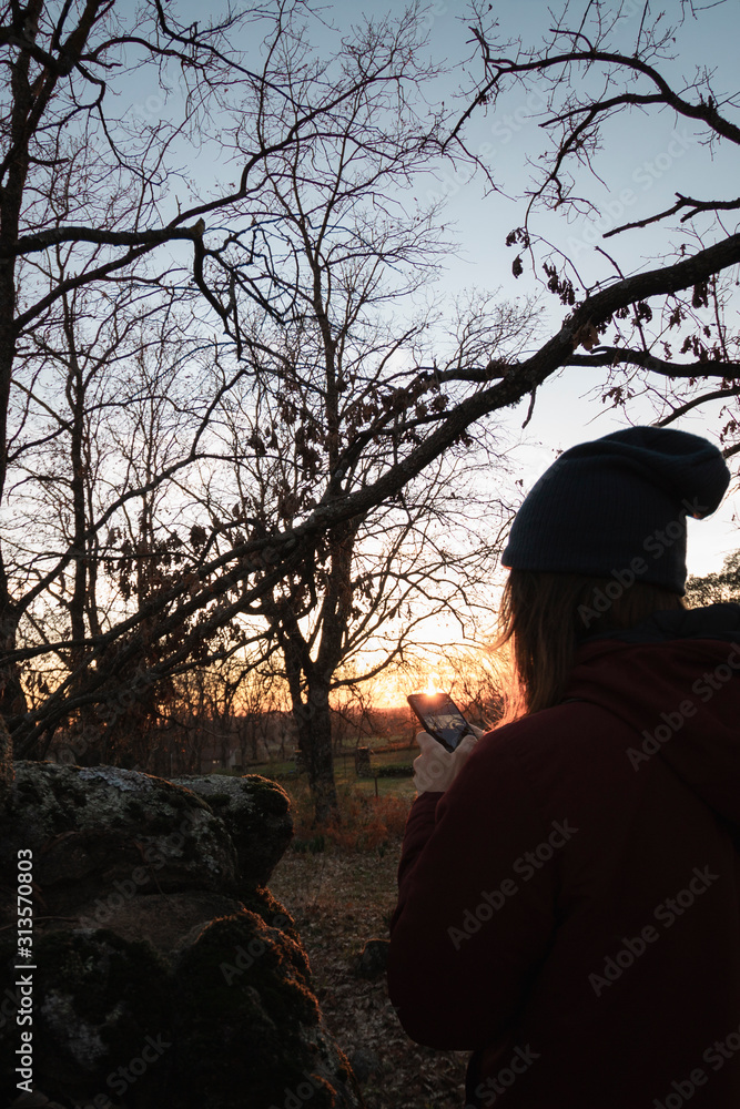 Chico con gorro mirando el smartphono al atardecer Chico con gorro mirando el smartphono al atardecer