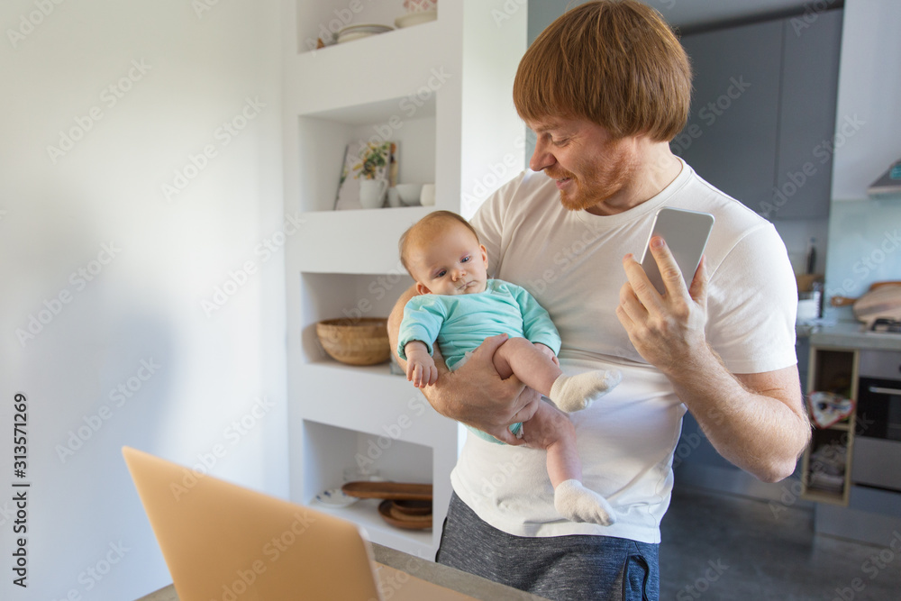 Obraz premium Cheerful new dad working at home, getting good news, sharing with baby daughter. Family portrait of red haired man and cute little child in home interior. Communication or baby care concept