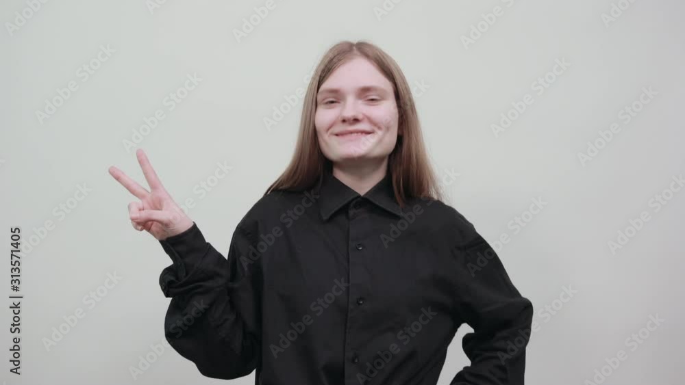 Cheerful attractive blonde woman in fashion black shirt isolated on gray background in studio doing victory symbol, smiling, keepung hand on belt. People sincere emotions, lifestyle concept. Cheerful attractive blonde woman in fashion black shirt isolated on gray background in studio doing victory symbol, smiling, keepung hand on belt. People sincere emotions, lifestyle concept.