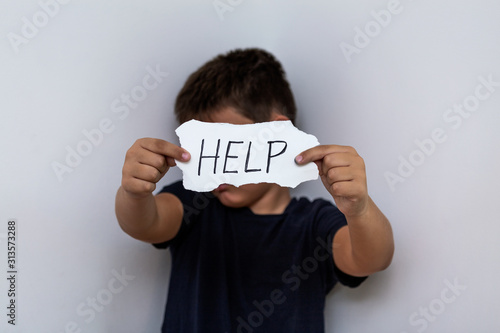 HELP, Teenager with help sign. Boy holding a paper with the inscription. Kid holding sheet of paper with word HELP on grey wall background.