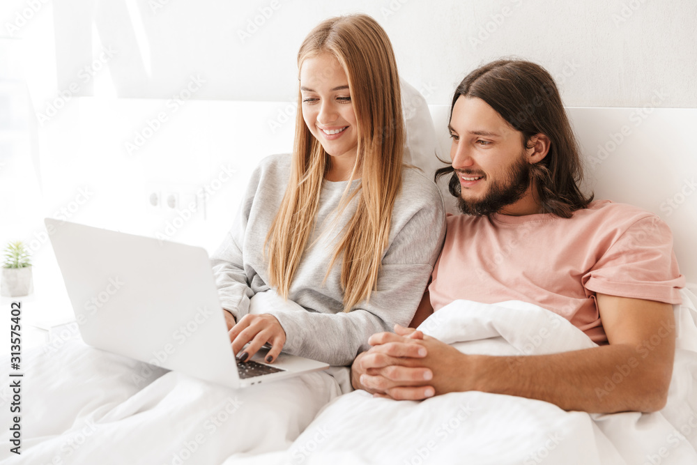 Loving couple in bed using laptop computer indoors at home. Loving couple in bed using laptop computer indoors at home.