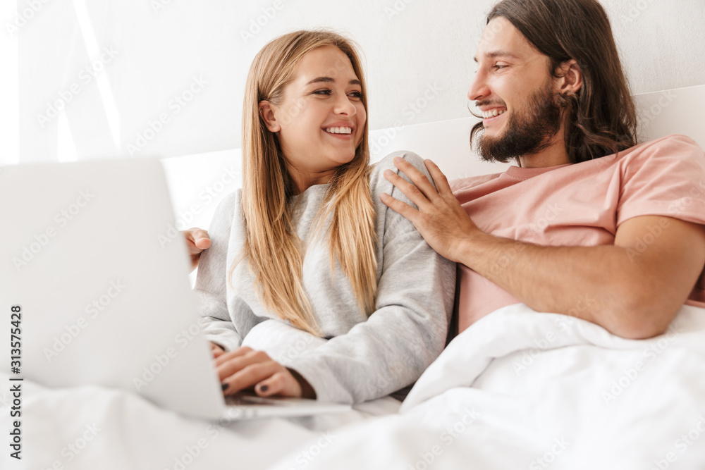 Loving couple in bed using laptop computer indoors at home. Loving couple in bed using laptop computer indoors at home.