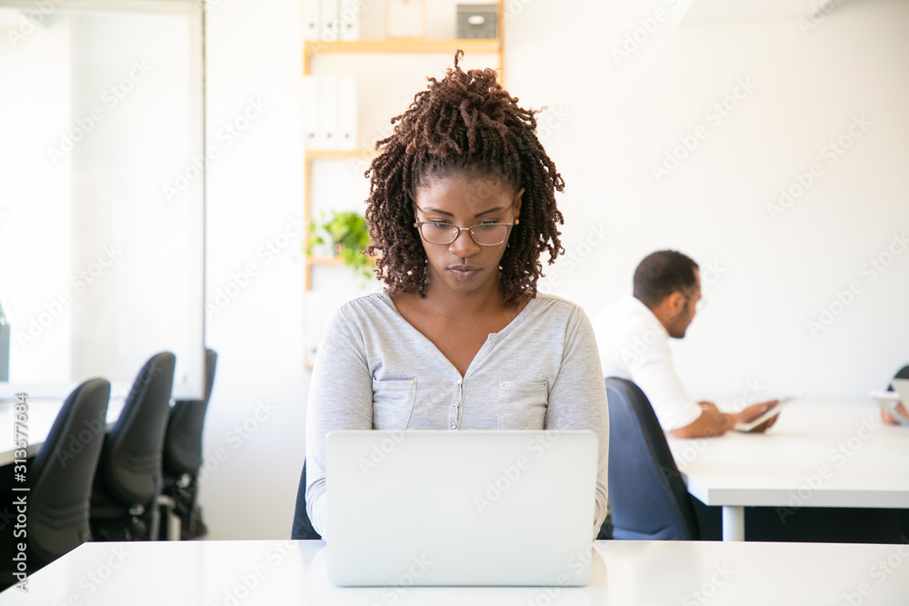 Focused young woman with dreadlocks typing on laptop. Front view of concentrated worker using laptop at office. Technology concept Focused young woman with dreadlocks typing on laptop. Front view of concentrated worker using laptop at office. Technology concept