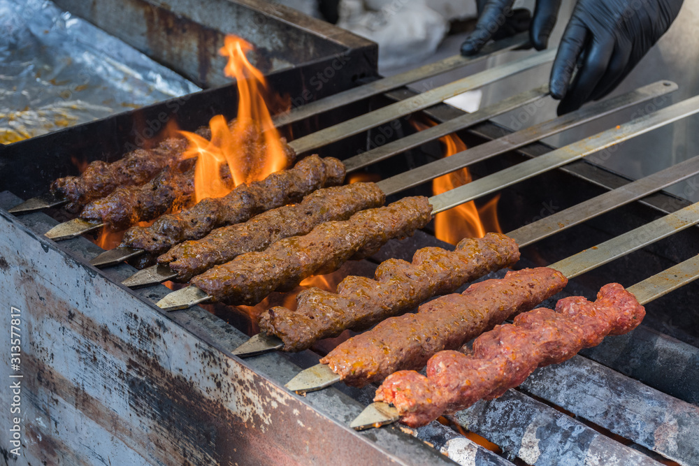 Fotka „Adana kebab (ground lamb minced meat on skewer on grill over  charcoal).Chef preparing traditional authentic Turkish shaworma. Middle  eastern cuisine. Handmade specialty street food market with spices“ ze  služby Stock