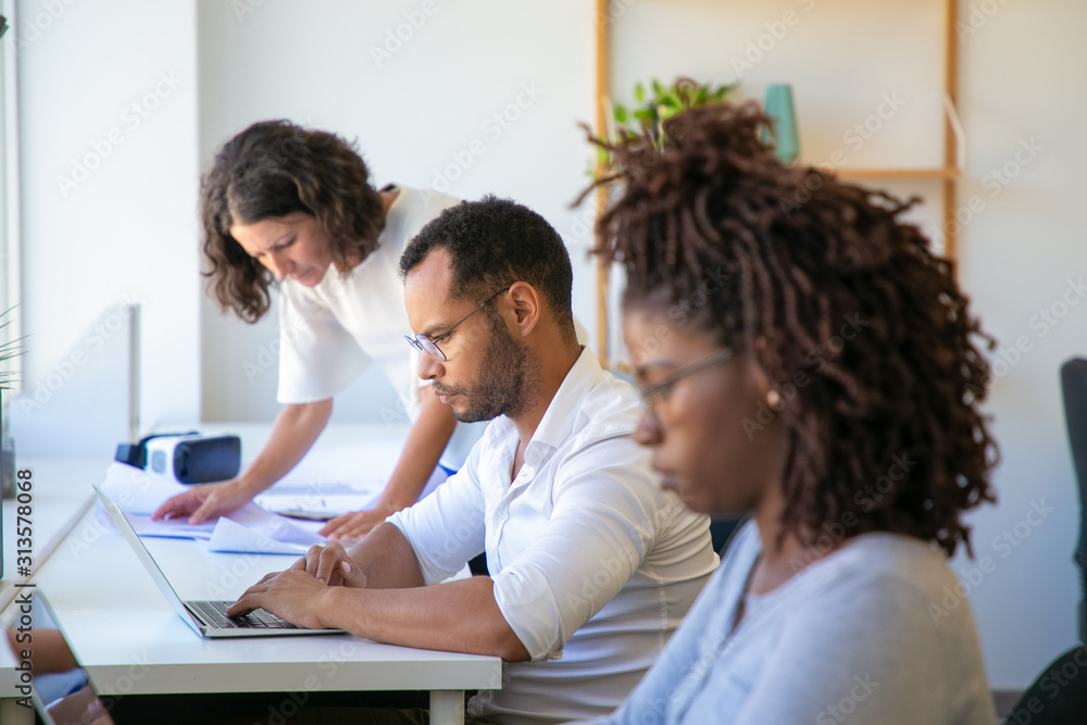 Focused young man in eyeglasses typing on laptop. Side view of concentrated worker using laptop at office. Technology concept Focused young man in eyeglasses typing on laptop. Side view of concentrated worker using laptop at office. Technology concept