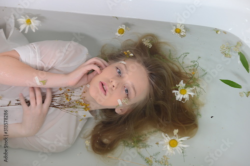 a girl in a white dress is lying in a bath with milk and flowers