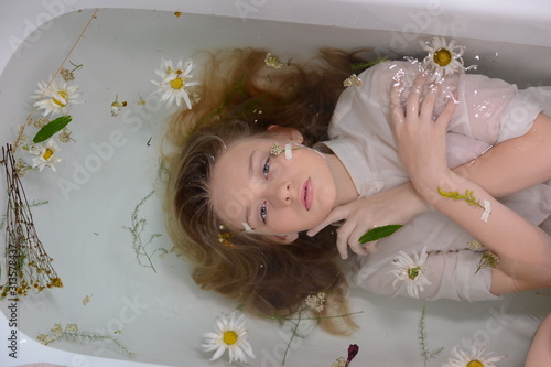a girl in a white dress is lying in a bath with milk and flowers
